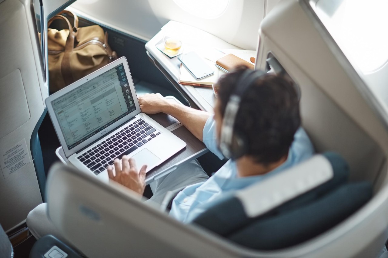 INF_JCL_C269Y16_E0 A male passenger is sitting inside a Business cabin seat on a Cathay Pacific aircraft with a computer on his lap.