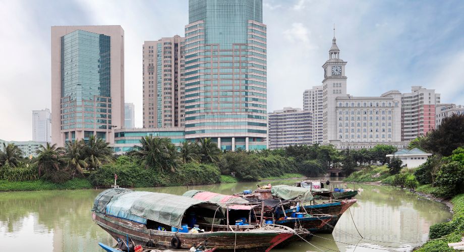 De vieilles embarcations en bois contrastant avec les gratte-ciel modernes d’Haikou en arrière-plan 