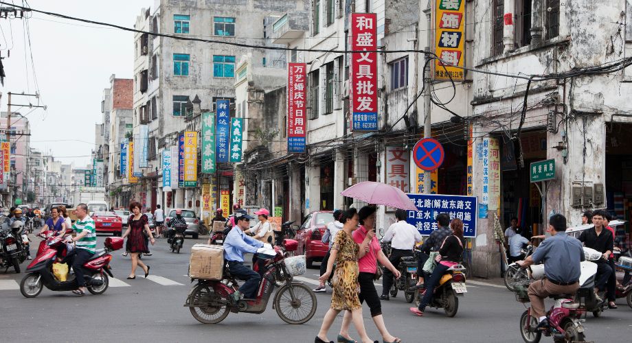 Deux femmes sous une ombrelle rose traversent une route bondée de scooters à Qilou Street, dans le quartier historique d’Haikou