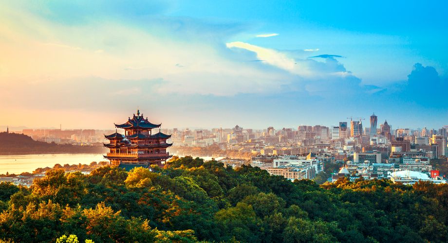 Vista de una pagoda y de colinas verdes con la ciudad de Hangzhou al fondo bajo un cielo azul