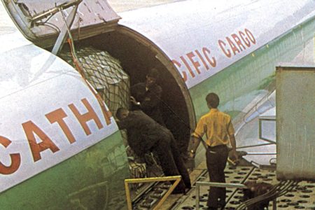 A grainy vintage photograph of a aircraft with 'Cathay Pacific Cargo'. Its door is opened while a man stands next to it.