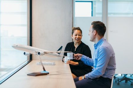 Zwei Kollegen unterhalten sich an einem Schreibtisch, auf dem ein Flugzeugmodell steht.