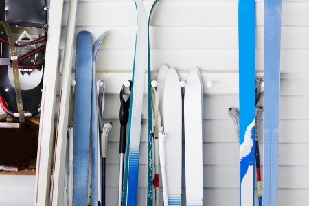 Close-up of a variety of skis and ski poles on a wall-mounted ski rack.
