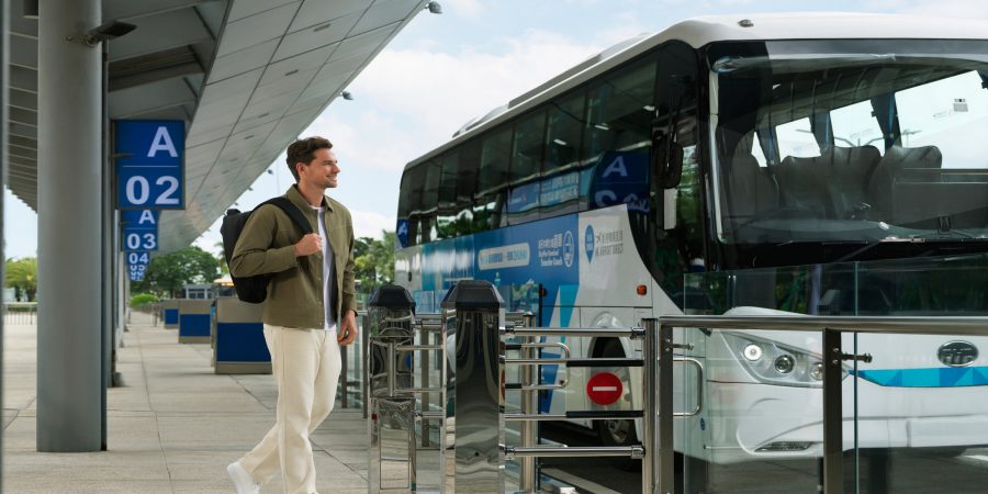  A back view shot of a passenger in a window seat of a shuttle bus. She is looking out to the road through the window.