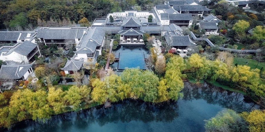 Aerial view of Four Seasons Hotel Hangzhou at West Lake surrounded by a serene pond and lush greenery.