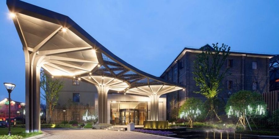 A nighttime view of a hotel entrance, featuring bright lights and elegant design, inviting guests to enter.