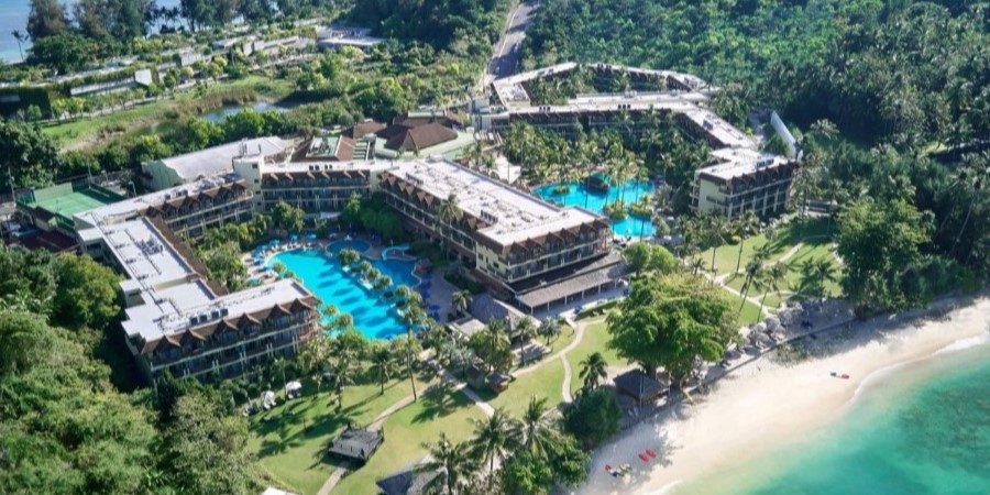 Aerial view of a beach resort, showcasing its layout and proximity to the sandy shore and ocean waves.