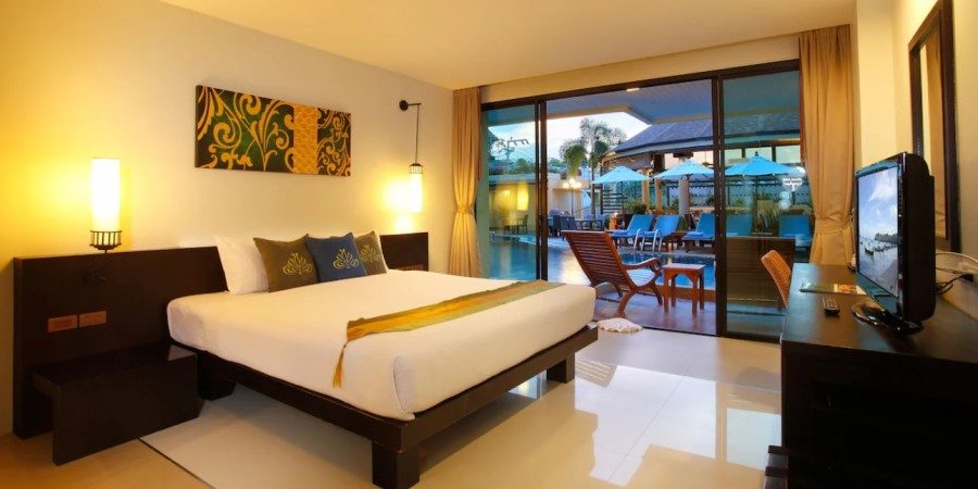 A hotel room featuring a large bed and a balcony with outdoor seating, offering a view of the surroundings.