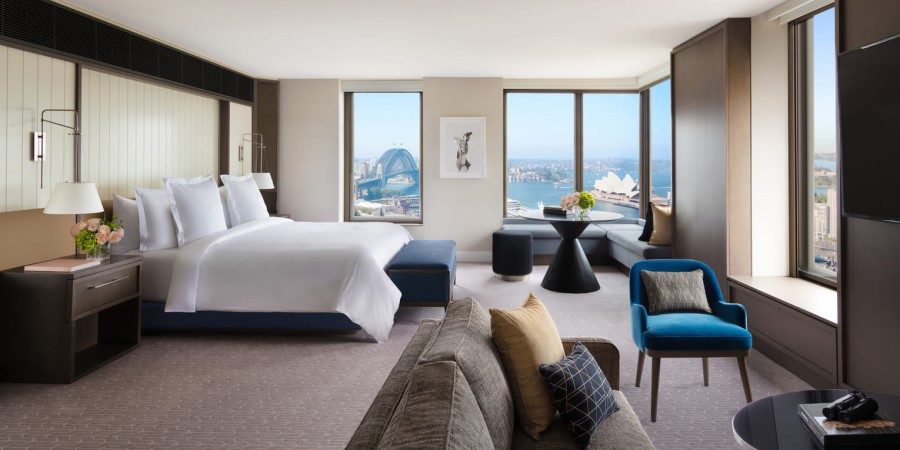 A hotel room featuring a stunning view of Sydney Harbour, showcasing the water and skyline through large windows.