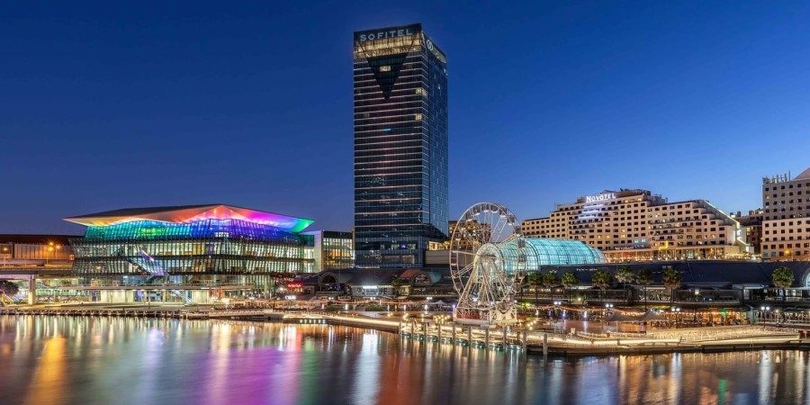 City skyline at night featuring a waterway and a brightly lit ferris wheel in the foreground.