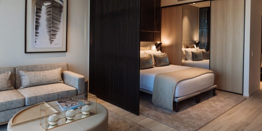 A modern bedroom featuring a neatly made bed, a stylish couch, and a large mirror reflecting the room's decor.