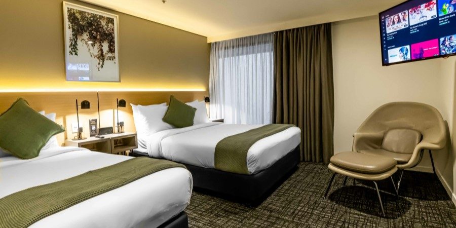Two beds in a hotel room with a television mounted on the wall, creating a cozy and inviting atmosphere.