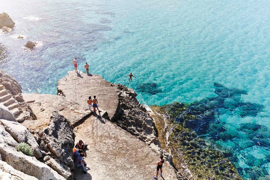 People jumping off a cliff into crystal clear blue waters
