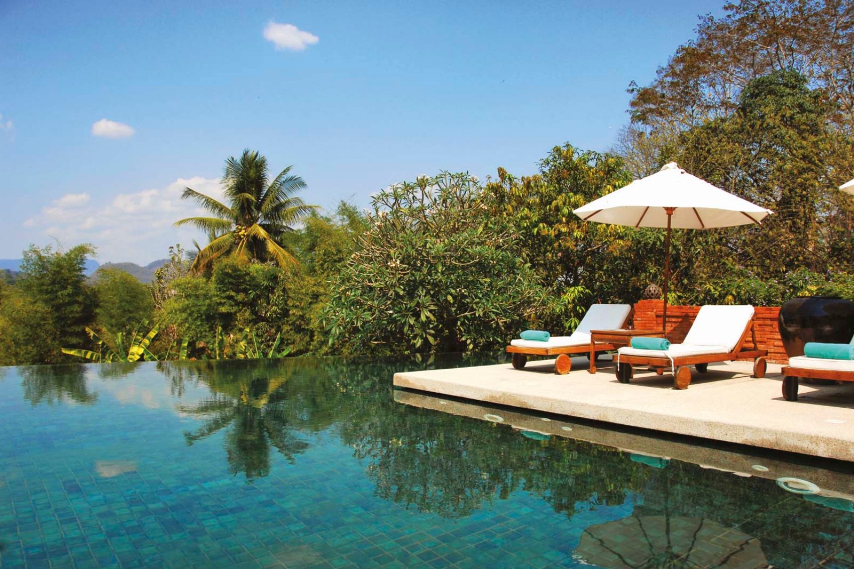 Deckchairs by a swimming pool surrounded by greenery