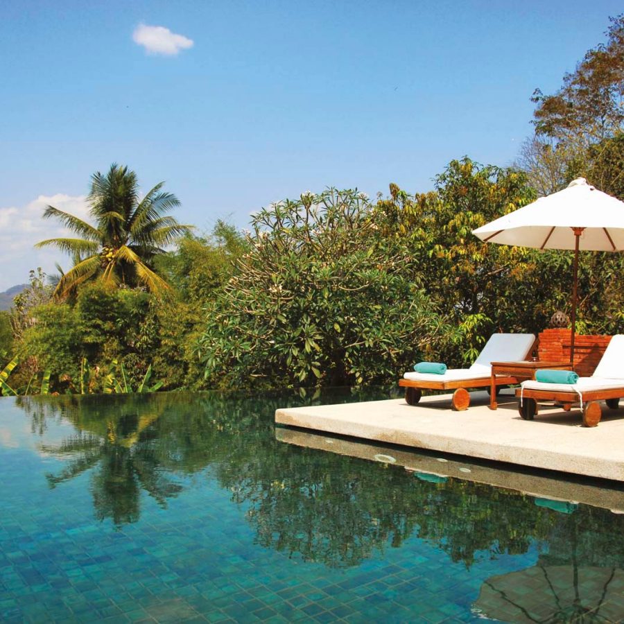 Deckchairs by a swimming pool surrounded by greenery
