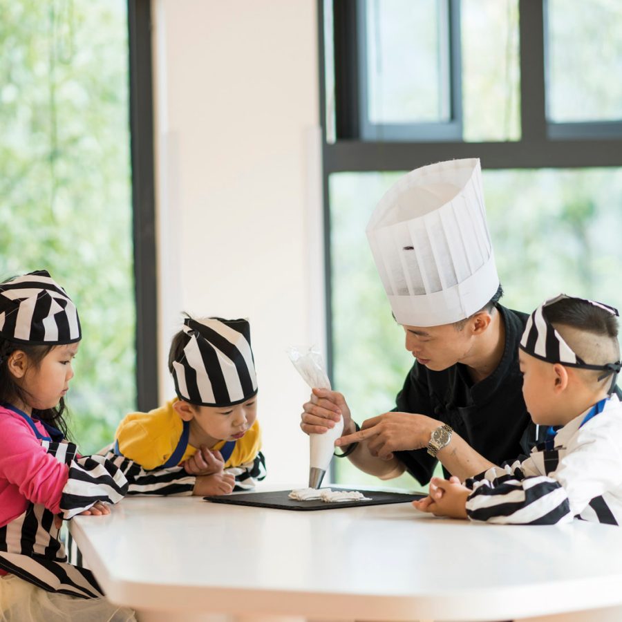 Pastry chef showing three kids how to use icing