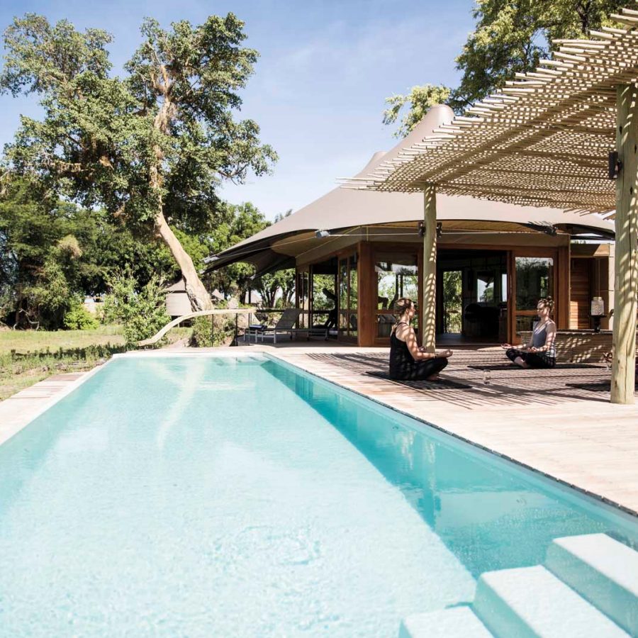 Yoga by a swimming pool surrounded by greenery