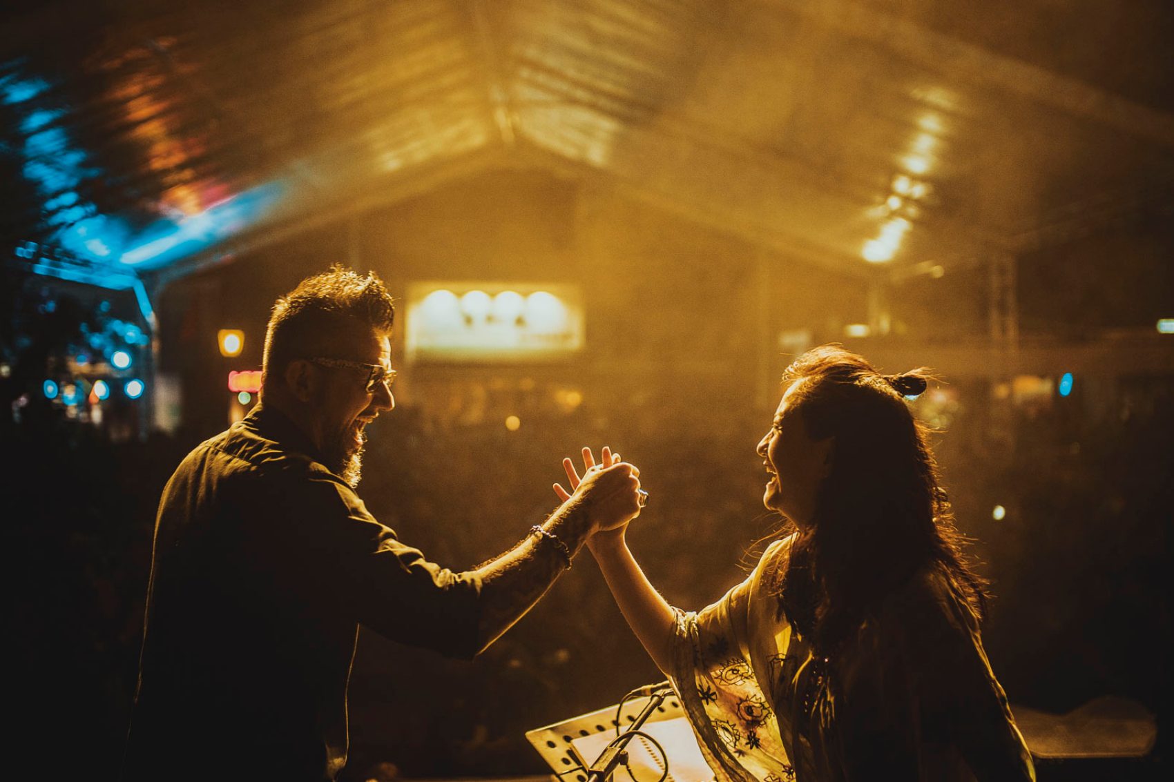 A man and woman smiling and shaking hands  on stage infront of a crowd at a live concert 