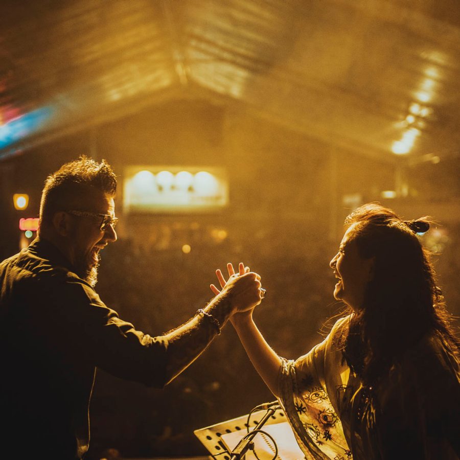 A man and woman smiling and shaking hands  on stage infront of a crowd at a live concert 