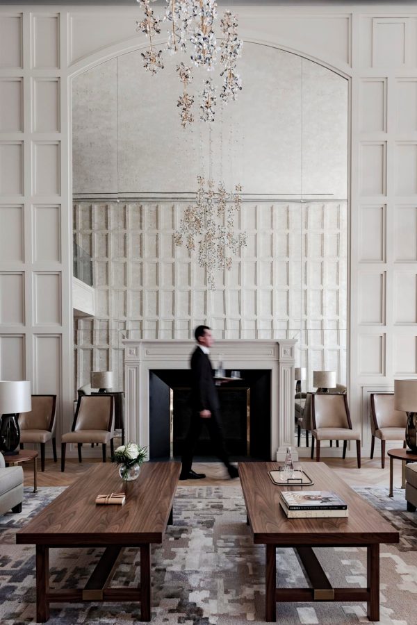A person in a suit walks across a room with white walls and wooden furniture.