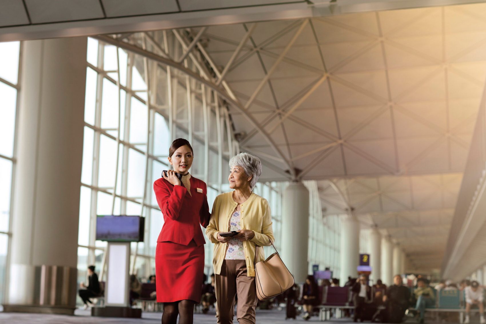 A Cathay Pacific crew member assisting an older lady at Hong Kong International Airport