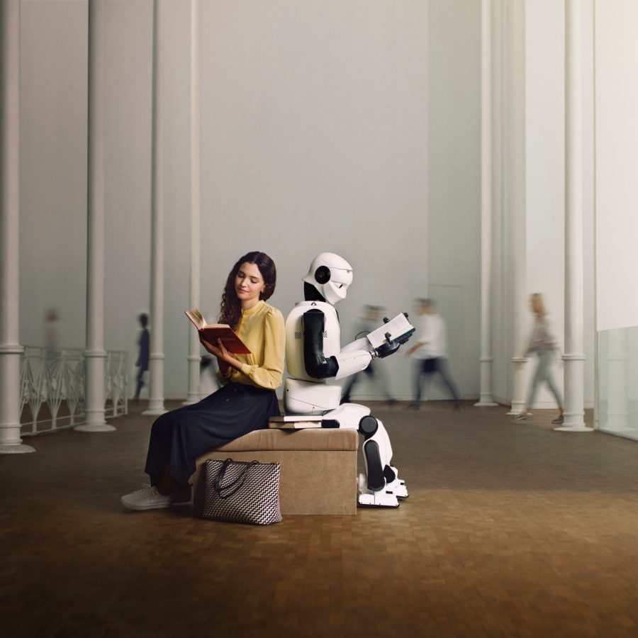 Lady and robot reading books sitting back to back in the middle of a large room