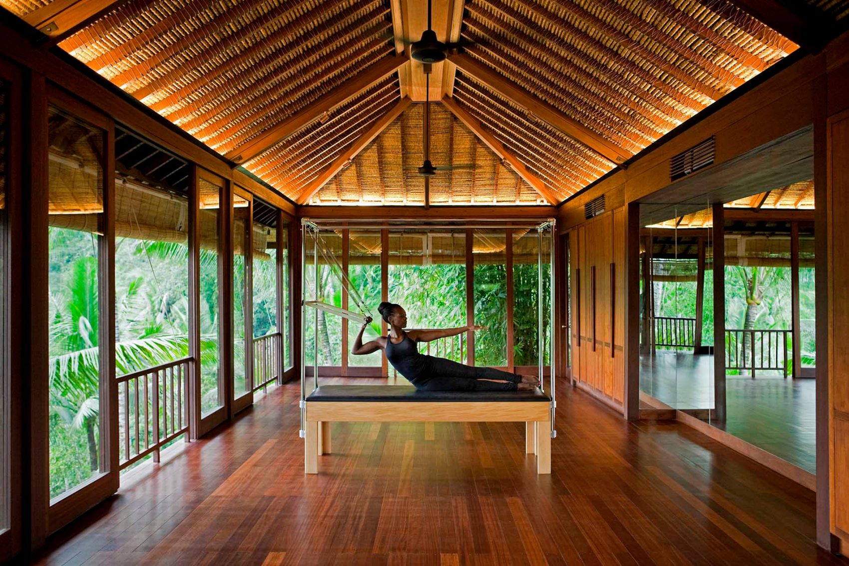 A woman doing pilates in a wooden bungalow in the forest surrounded by green foliage