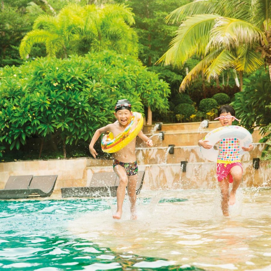 Two kids running along a pool