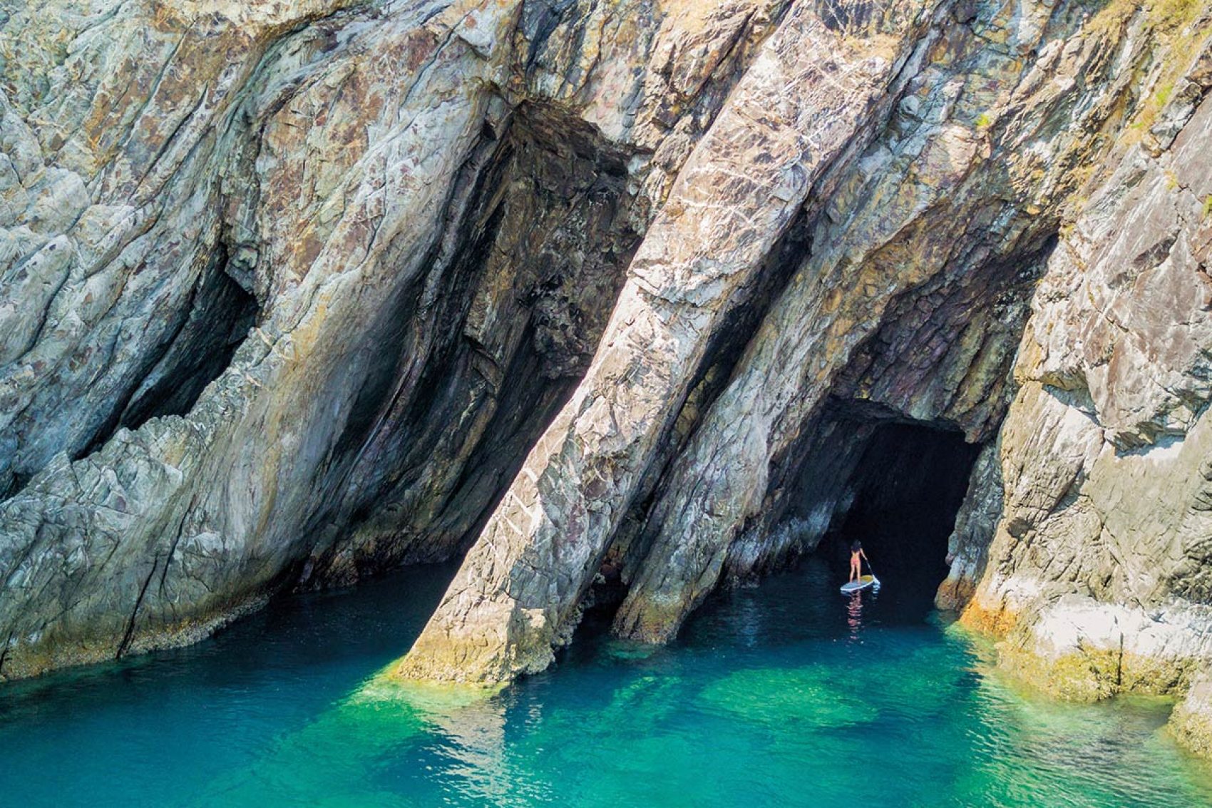 Stand up paddle boarding into a cave on blue wats