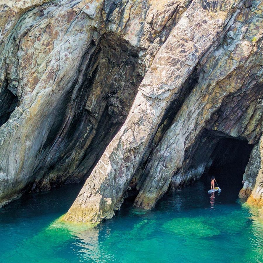 Stand up paddle boarding into a cave on blue wats