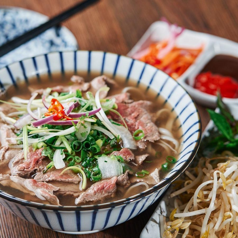 A bowl of Vietnamese Pho is placed on a table alongside bean sprouts.