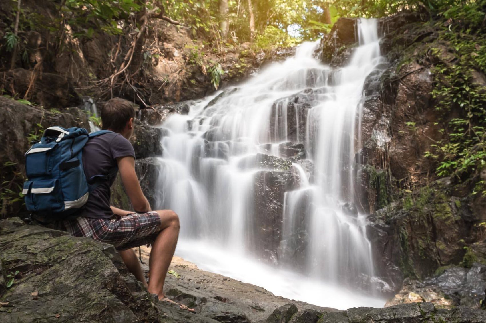  A man sitting on the stone and looking on the stunning Ton Sai waterfall in Phuket, Thailand