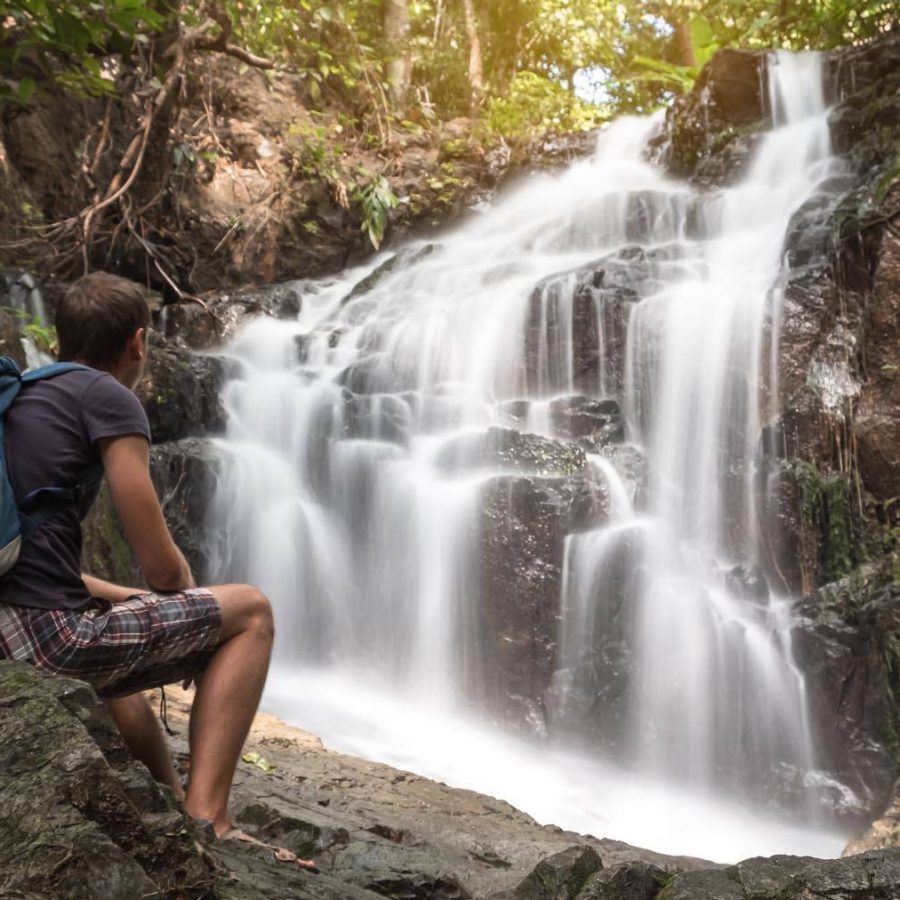  A man sitting on the stone and looking on the stunning Ton Sai waterfall in Phuket, Thailand