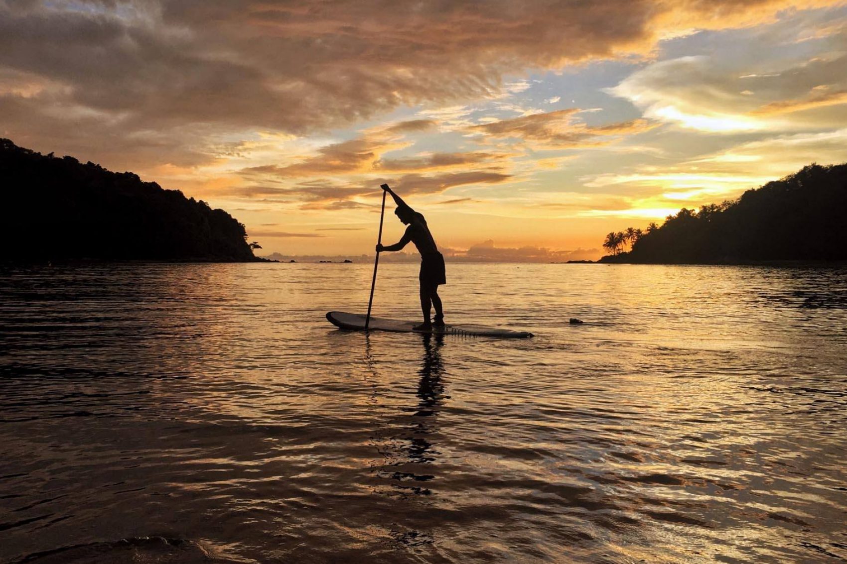 A tourist is touring the sea in Phuket on a stand-up paddleboard during sunrise