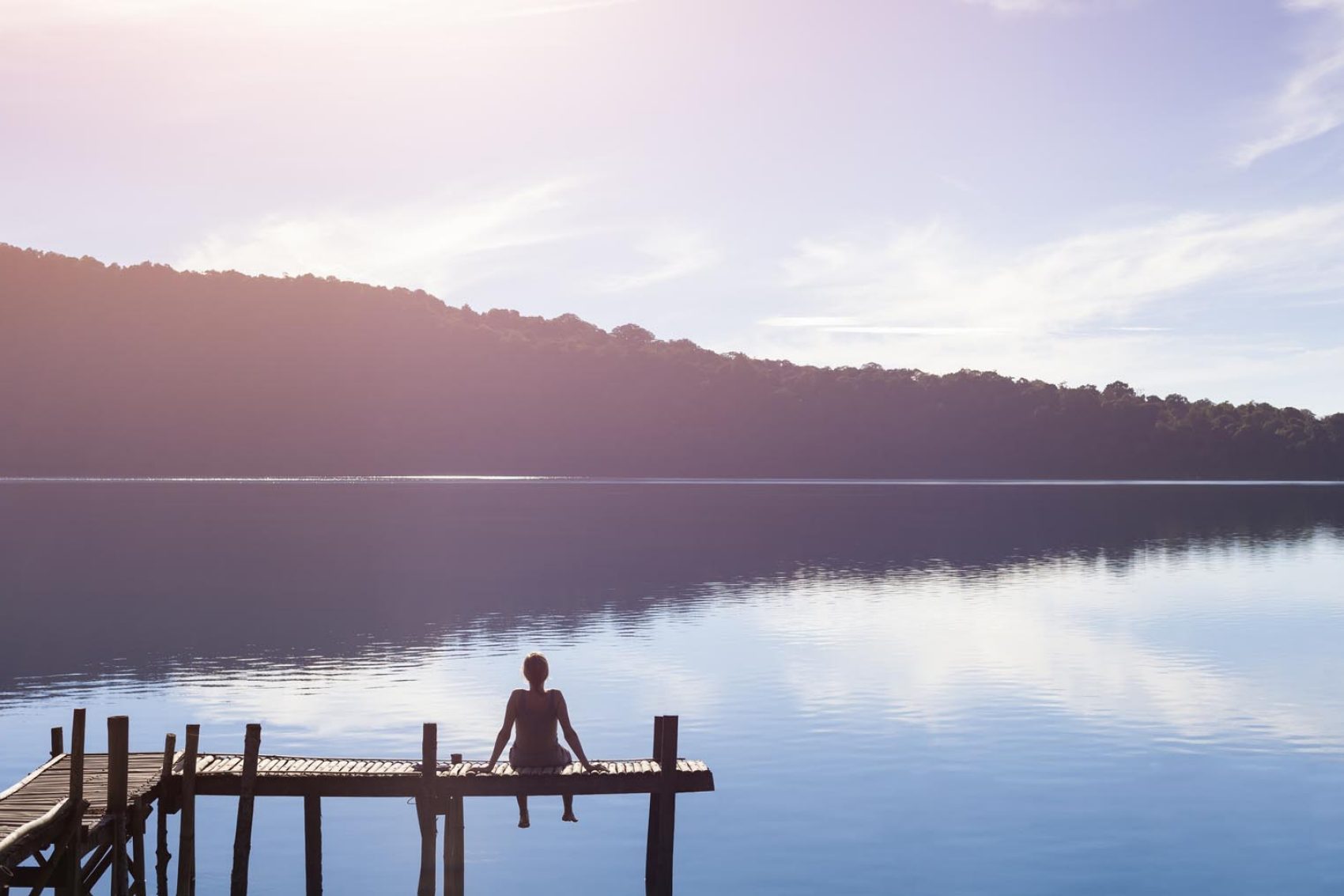 Person sitting on a pier in front of a serene lake. Credit: iStock