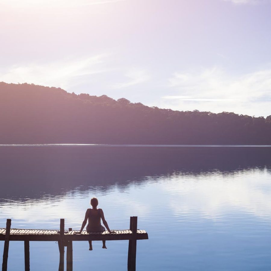 Person sitting on a pier in front of a serene lake. Credit: iStock