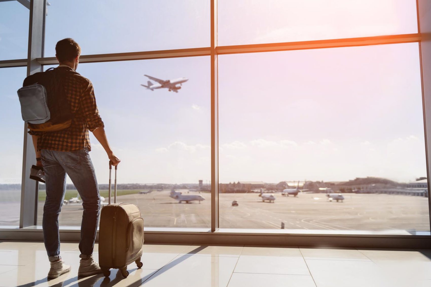 Man with suitcase watching plane take off in the distance. Credit: iStock