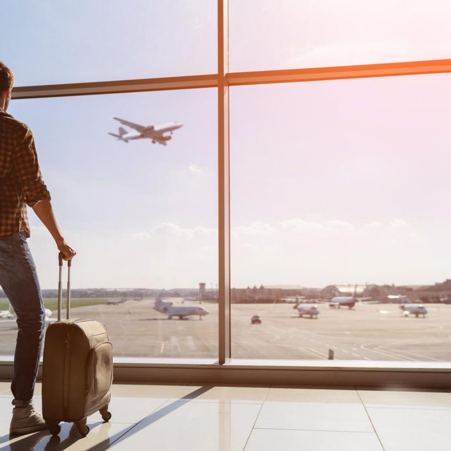 Man with suitcase watching plane take off in the distance. Credit: iStock