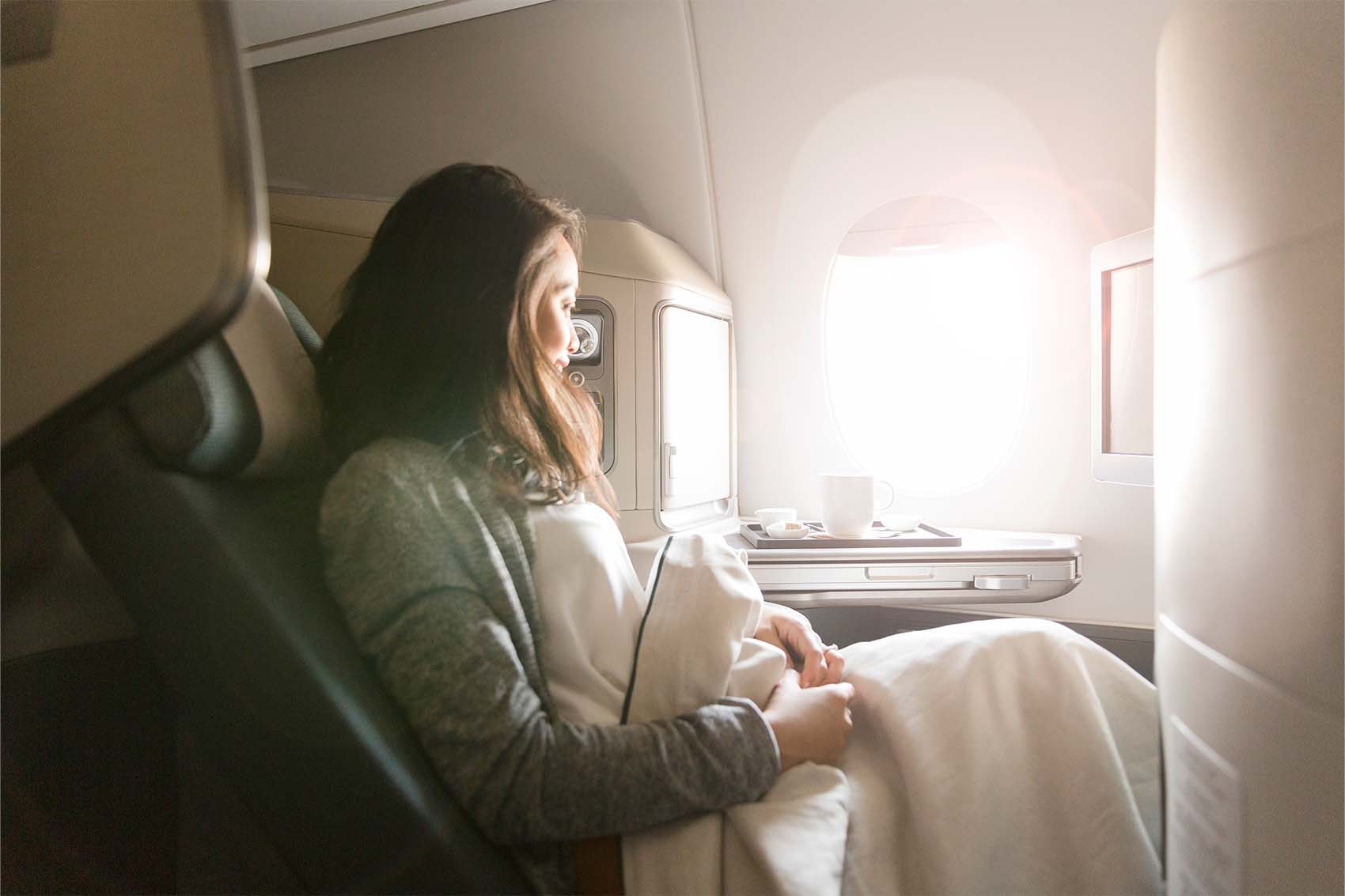 Passenger enjoying business class on plane under blanket, looking out the window