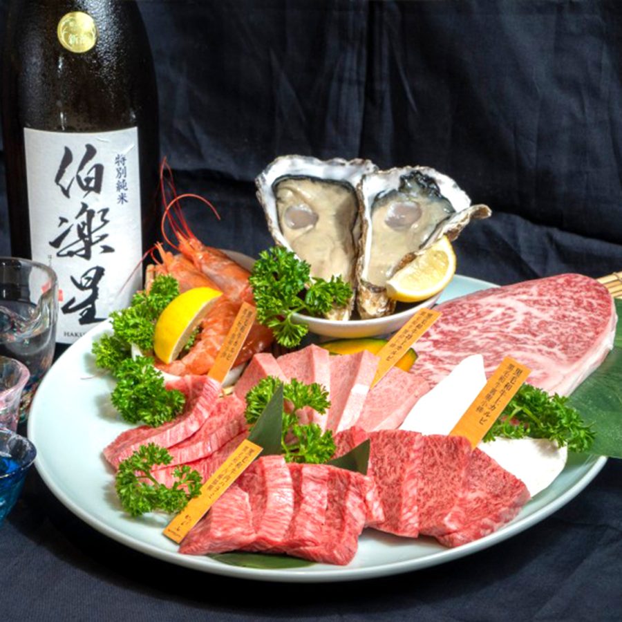 Plate of meat and seafood next to a bottle of sake