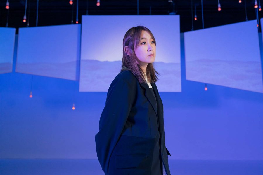 Ivana Wong looks into the distance against a blue backdrop.