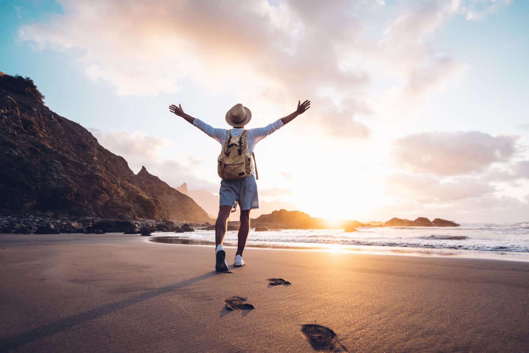 A man raising his arms at the sunset on a beach. Credit: Getty Images