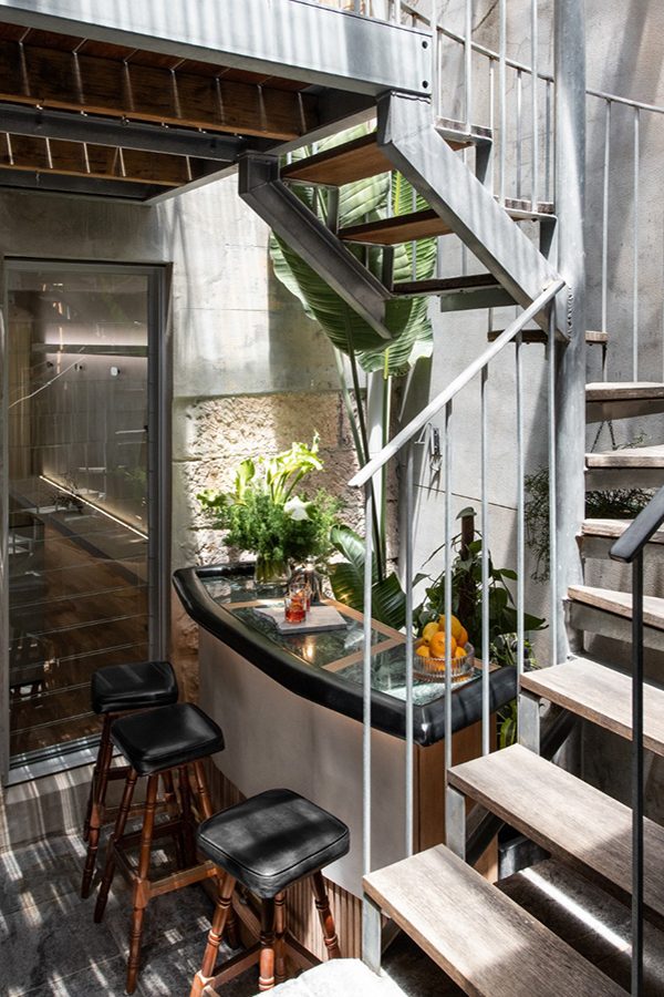 An art deco minibar decorated with green plants and a staircase in the courtyard of bespoke tailor shop Belance in Paddington, Australia