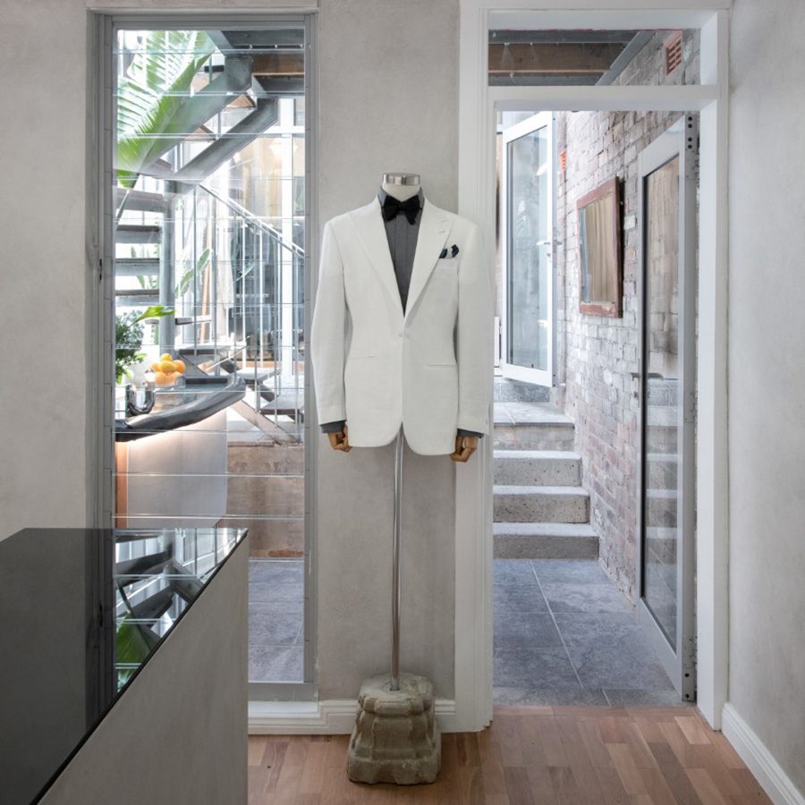 An interior view of Belance store facing the courtyard, showcasing a white bespoke suit and bow tie on display