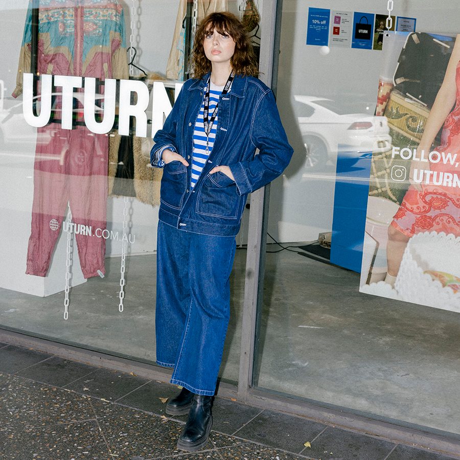 A woman wearing denim jacket and pants standing infront of the shop window of vintage fashion store Uturn in Surry Hills, Sydney, Australia