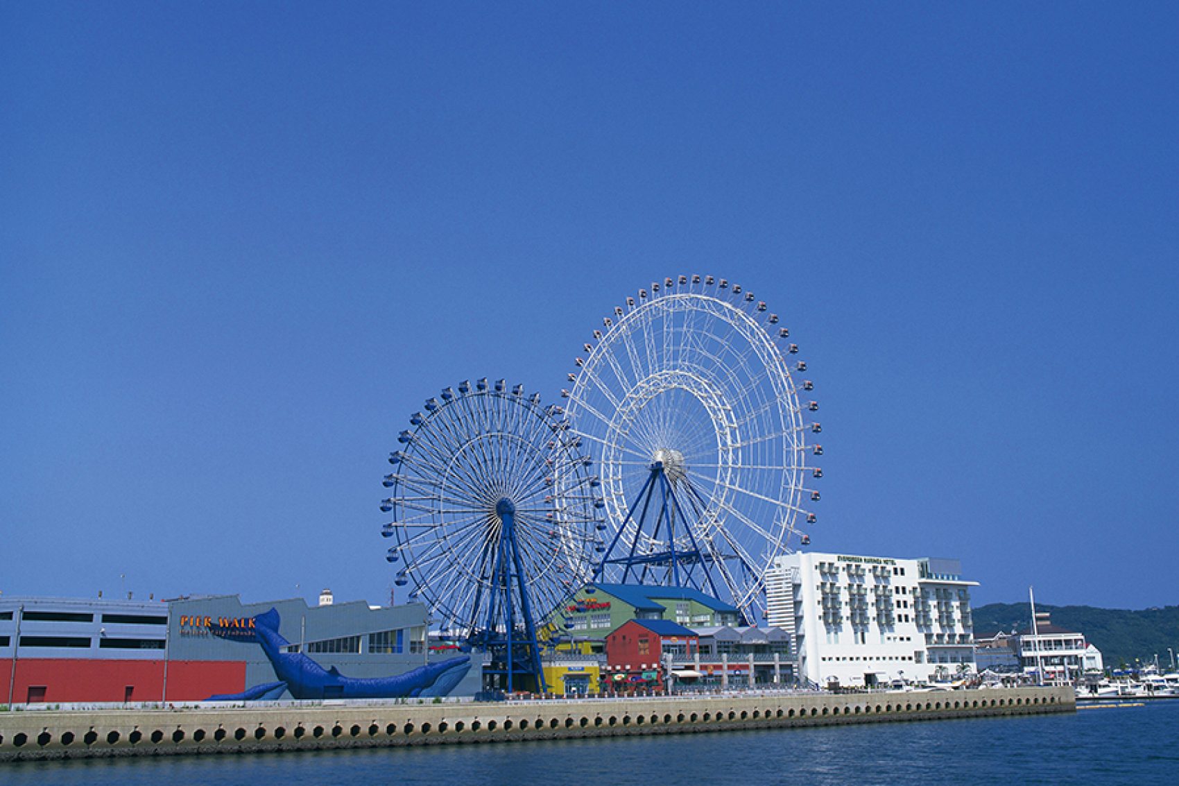 A seaside view of Marinoa City Fukuoka Outlet mall by the pier featuring two ferris wheels outside during daytime 