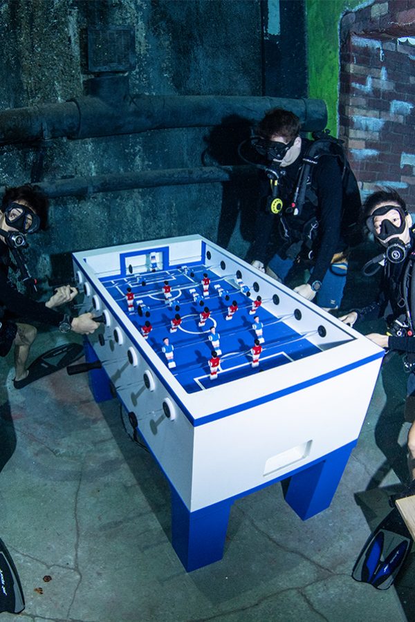 A group of scuba divers playing a game of foosball underwater in Deep Dive Dubai