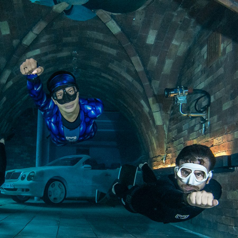 Two divers wearing scuba gear and snorkling goggles swimming through a tunnel in Deep Dive Dubai