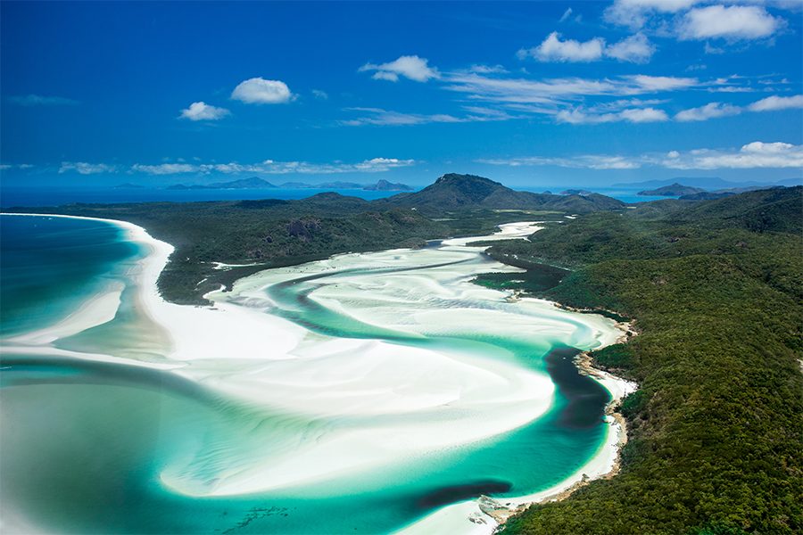 An aerial view of white and blue-green water surrounded by rolling hills in an island in Great Barrier Reef, Australia