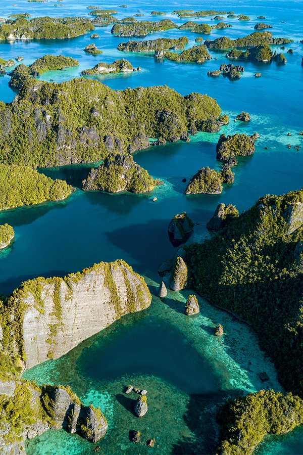 An aerial view of a blue-green lagoon surrounded by many small islands in Raja Ampat, Indonesia 